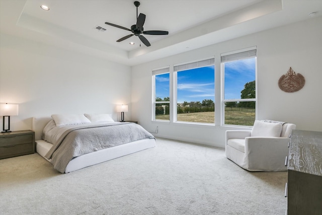 bedroom with ceiling fan, a tray ceiling, and light colored carpet