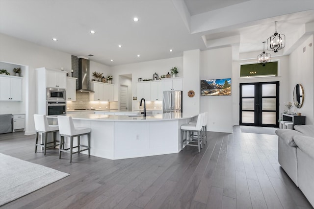 kitchen featuring white cabinetry, a kitchen breakfast bar, a large island with sink, stainless steel appliances, and wall chimney exhaust hood