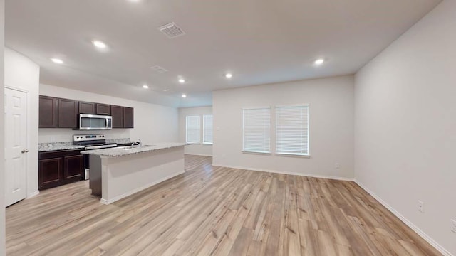 kitchen with sink, dark brown cabinetry, light stone counters, a center island with sink, and light wood-type flooring