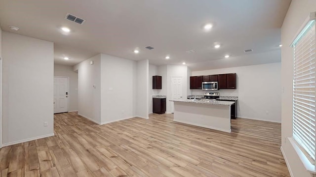 kitchen featuring a kitchen island with sink, light stone counters, light hardwood / wood-style flooring, and appliances with stainless steel finishes