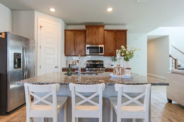 kitchen featuring a breakfast bar area, dark stone countertops, backsplash, stainless steel appliances, and light hardwood / wood-style floors