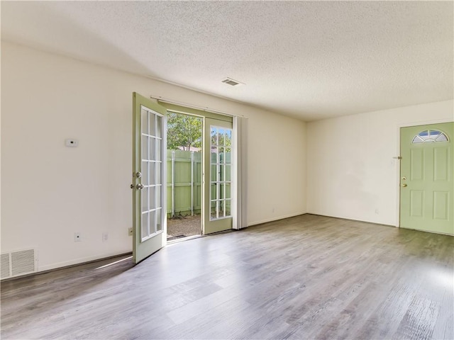 empty room featuring french doors, a textured ceiling, and light hardwood / wood-style flooring