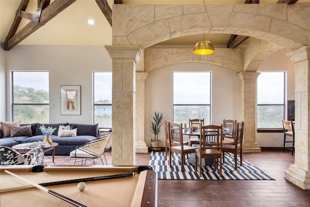 dining area featuring a towering ceiling, decorative columns, dark hardwood / wood-style floors, and beamed ceiling