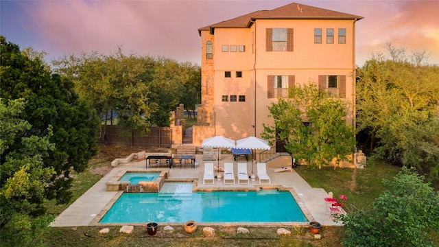 back house at dusk with a pool with hot tub and a patio area