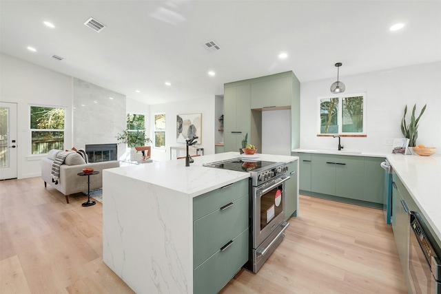 kitchen with a tile fireplace, appliances with stainless steel finishes, sink, a center island with sink, and light hardwood / wood-style flooring