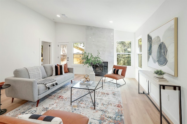 living room featuring high vaulted ceiling, light hardwood / wood-style floors, and a tile fireplace