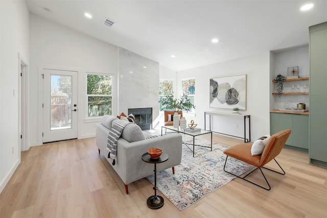 living room with vaulted ceiling, a tile fireplace, and light hardwood / wood-style flooring