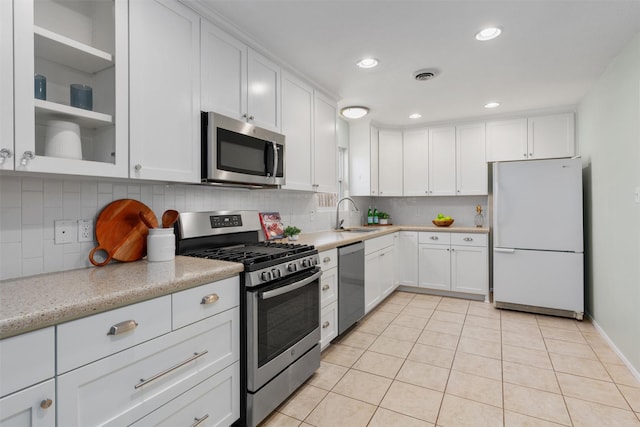 kitchen with appliances with stainless steel finishes, white cabinetry, sink, backsplash, and light tile patterned floors