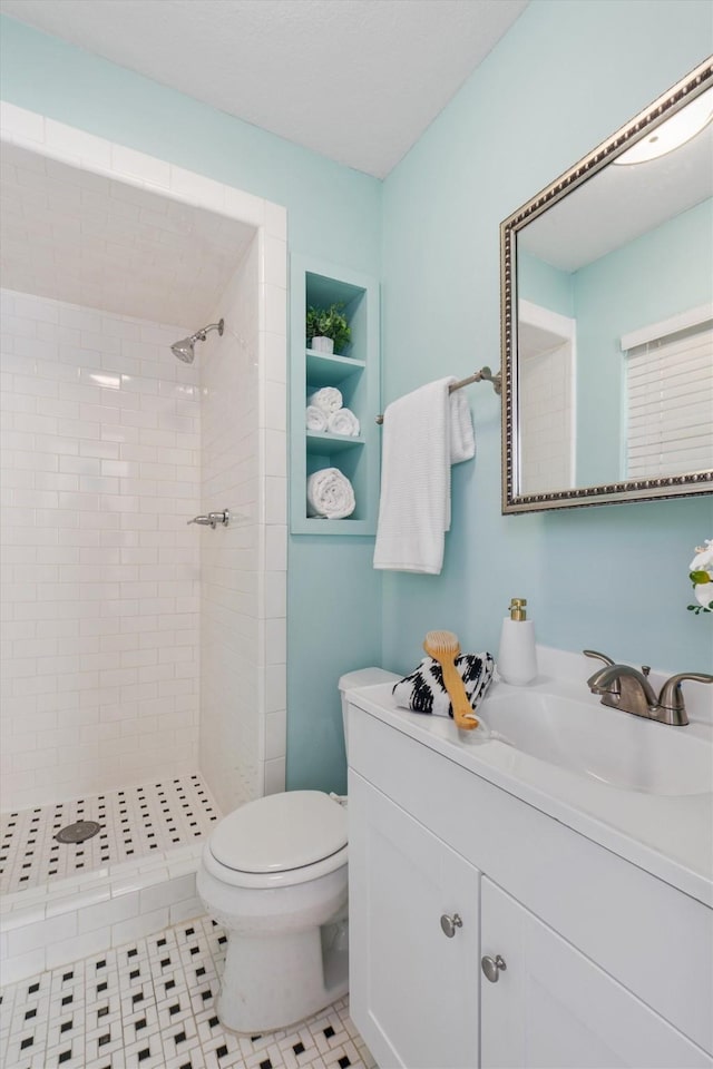 bathroom with toilet, a tile shower, vanity, and built in shelves