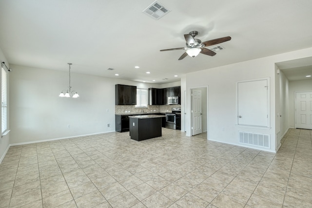 kitchen with hanging light fixtures, appliances with stainless steel finishes, a kitchen island, ceiling fan with notable chandelier, and backsplash