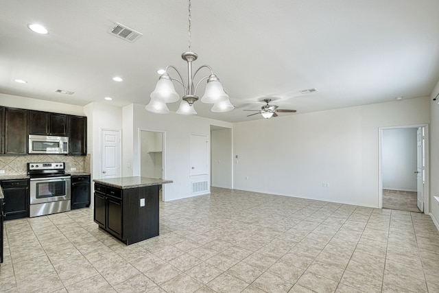 kitchen featuring appliances with stainless steel finishes, hanging light fixtures, a center island, light stone countertops, and decorative backsplash