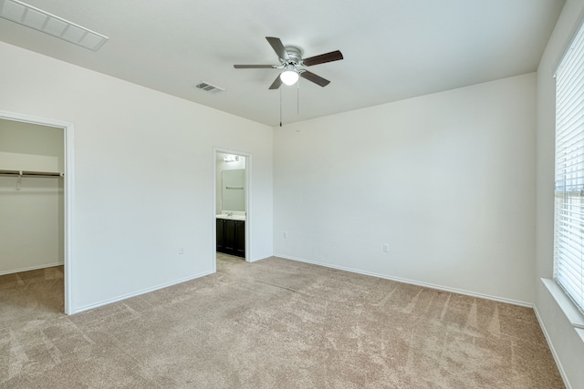 unfurnished bedroom featuring ceiling fan, a walk in closet, light carpet, and a closet