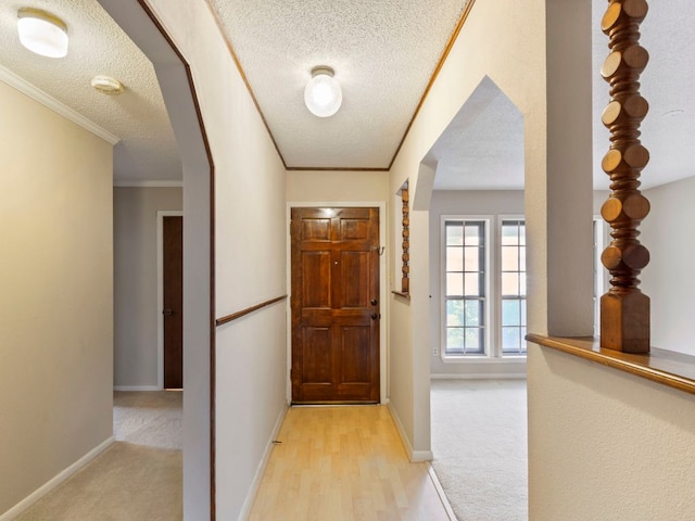 doorway to outside with a textured ceiling, baseboards, arched walkways, ornamental molding, and light wood-style floors