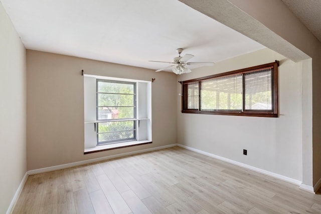 spare room with plenty of natural light, light wood-type flooring, ceiling fan, and baseboards