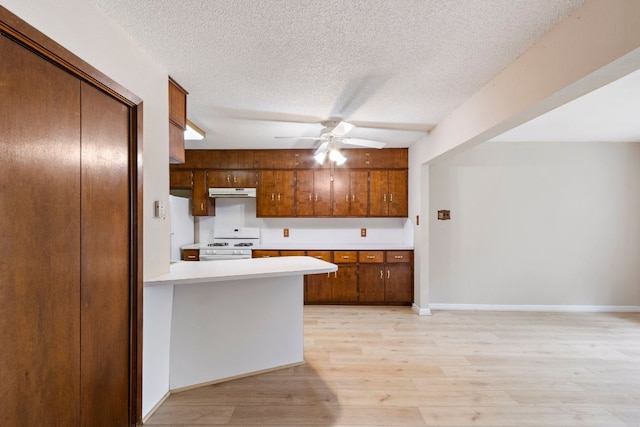 108 Fairlane Dr, Round Rock, TX 78664 - kitchen featuring white gas range oven, light countertops, a textured ceiling, under cabinet range hood, and brown cabinetry