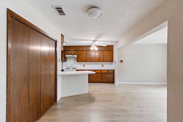 kitchen with white range with gas stovetop, a textured ceiling, under cabinet range hood, light countertops, and brown cabinets