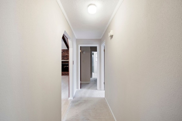 hallway featuring baseboards, light carpet, ornamental molding, and a textured ceiling