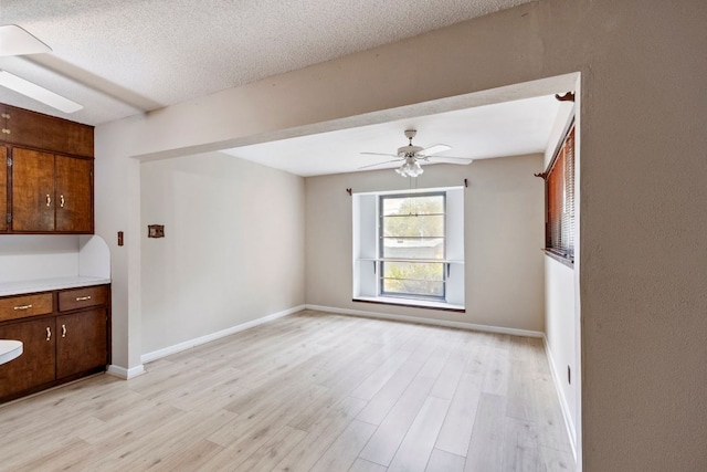 unfurnished living room with light wood-type flooring, a ceiling fan, baseboards, and a textured ceiling