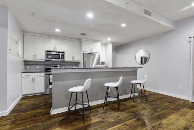 kitchen with dark wood-type flooring, a breakfast bar, appliances with stainless steel finishes, white cabinetry, and tasteful backsplash