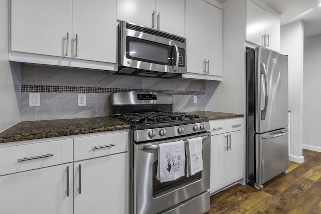 kitchen with appliances with stainless steel finishes, white cabinetry, dark stone countertops, dark hardwood / wood-style floors, and tasteful backsplash