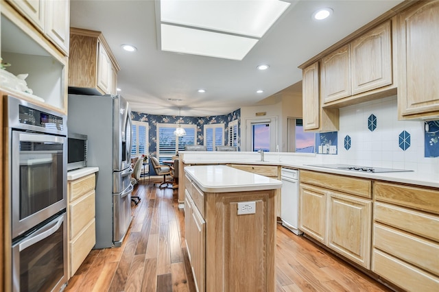 kitchen with appliances with stainless steel finishes, a center island, light brown cabinetry, and decorative light fixtures