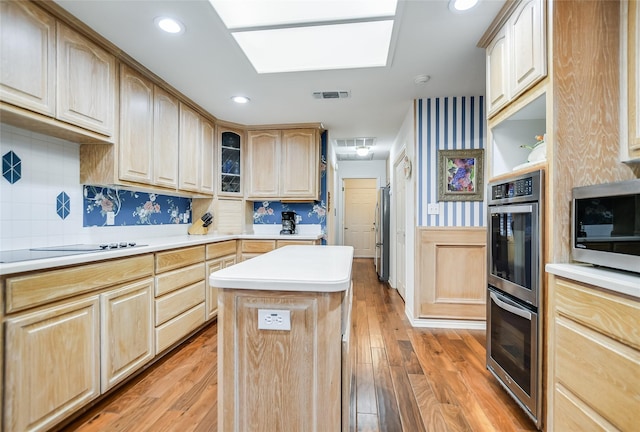 kitchen featuring backsplash, stainless steel appliances, a kitchen island, light wood-type flooring, and light brown cabinets