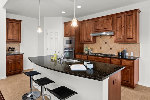 kitchen featuring appliances with stainless steel finishes, pendant lighting, sink, dark stone countertops, and a center island with sink