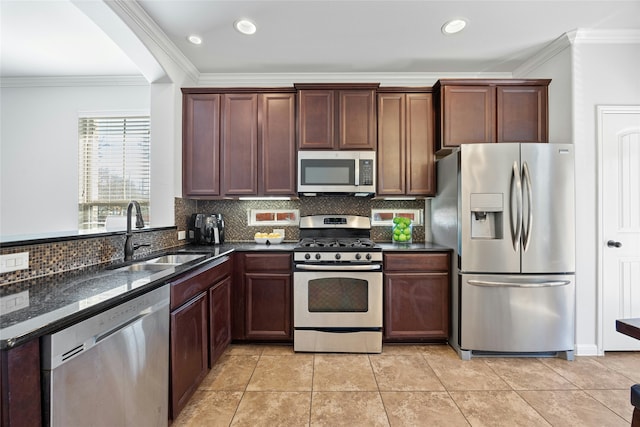 kitchen featuring sink, light tile patterned floors, ornamental molding, appliances with stainless steel finishes, and dark stone counters