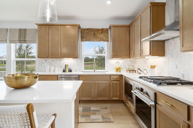 kitchen featuring sink, appliances with stainless steel finishes, pendant lighting, wall chimney range hood, and backsplash