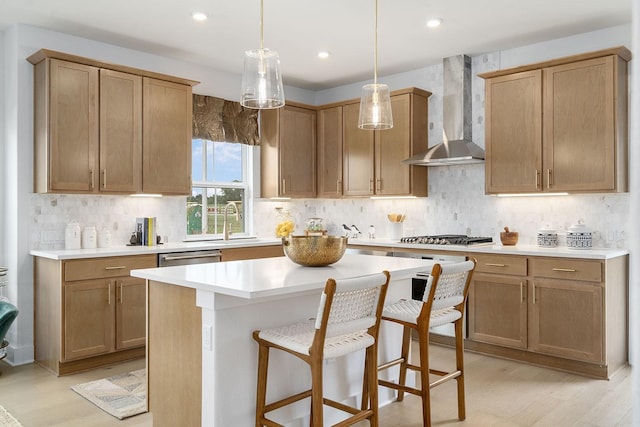 kitchen with wall chimney exhaust hood, a breakfast bar, a kitchen island, stainless steel appliances, and light hardwood / wood-style floors