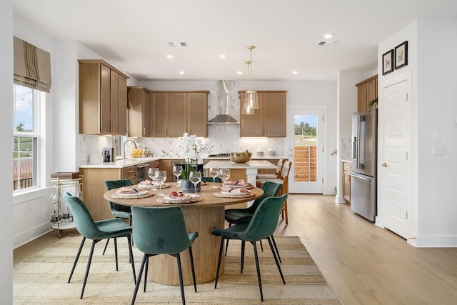 kitchen featuring decorative light fixtures, a center island, wall chimney exhaust hood, stainless steel appliances, and light hardwood / wood-style flooring