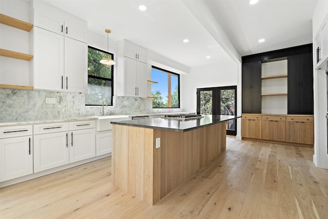 kitchen with a kitchen island, sink, white cabinets, hanging light fixtures, and light hardwood / wood-style floors