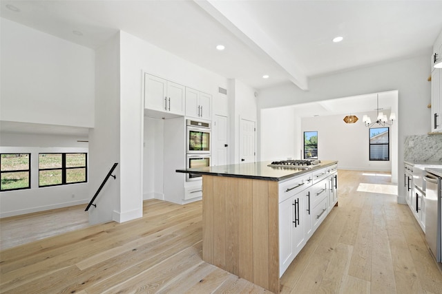 kitchen with a center island, light wood-type flooring, appliances with stainless steel finishes, beam ceiling, and white cabinets