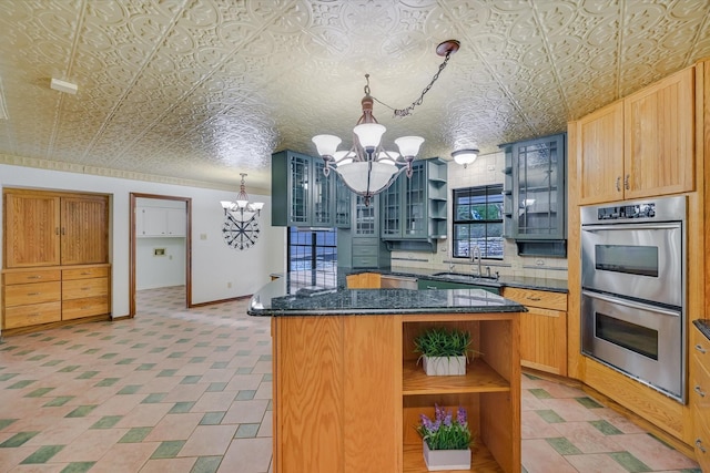 kitchen featuring a kitchen island, sink, dark stone countertops, a notable chandelier, and stainless steel double oven