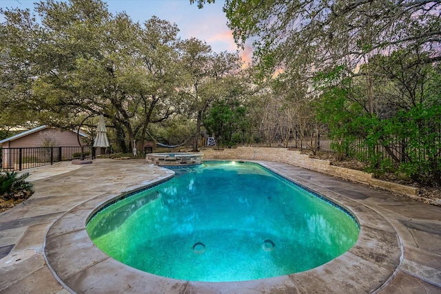 pool at dusk with a patio and an in ground hot tub