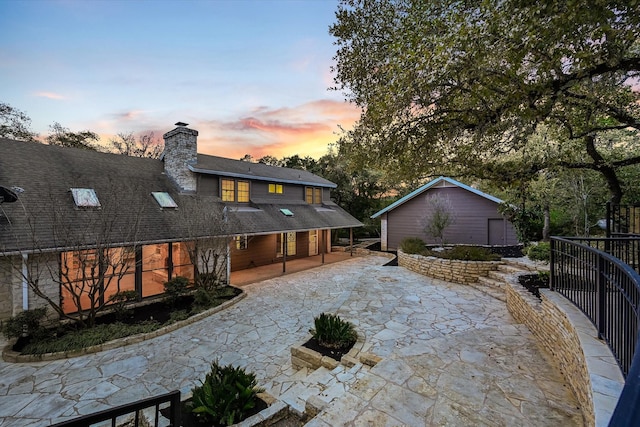 back house at dusk featuring a patio and an outdoor structure