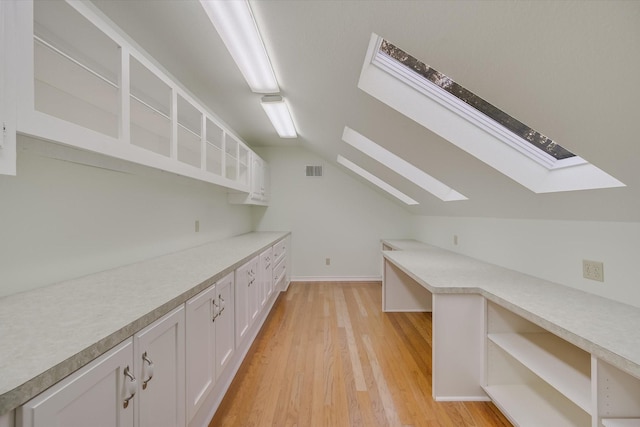 interior space with white cabinetry, lofted ceiling with skylight, and light hardwood / wood-style floors