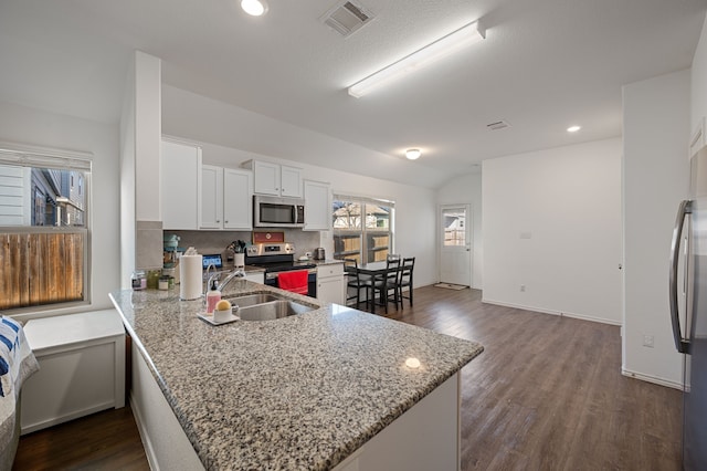 kitchen featuring lofted ceiling, appliances with stainless steel finishes, white cabinetry, light stone counters, and kitchen peninsula