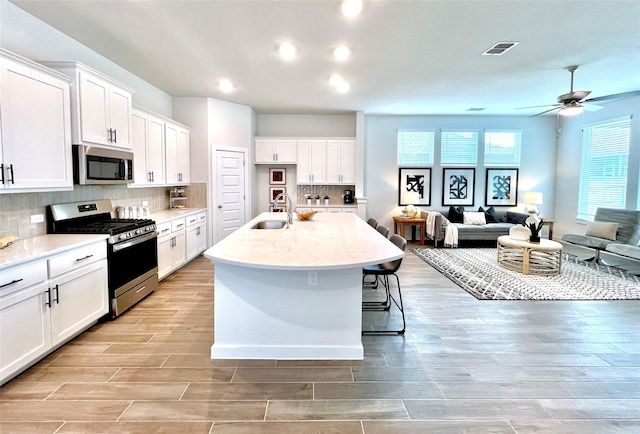 kitchen with sink, tasteful backsplash, an island with sink, stainless steel appliances, and white cabinets