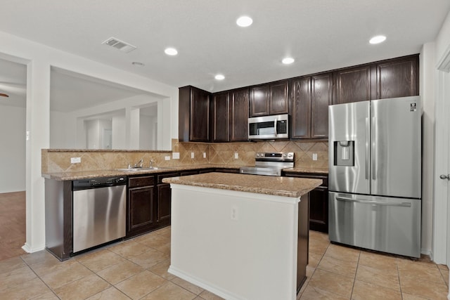 kitchen with stainless steel appliances, a kitchen island, light tile patterned floors, and light stone counters