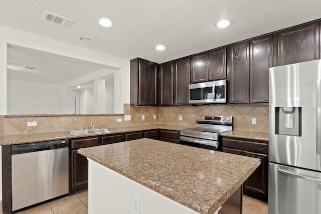 kitchen with sink, light tile patterned floors, stainless steel appliances, light stone counters, and a kitchen island