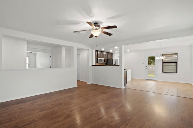 unfurnished living room with ceiling fan with notable chandelier and light hardwood / wood-style floors