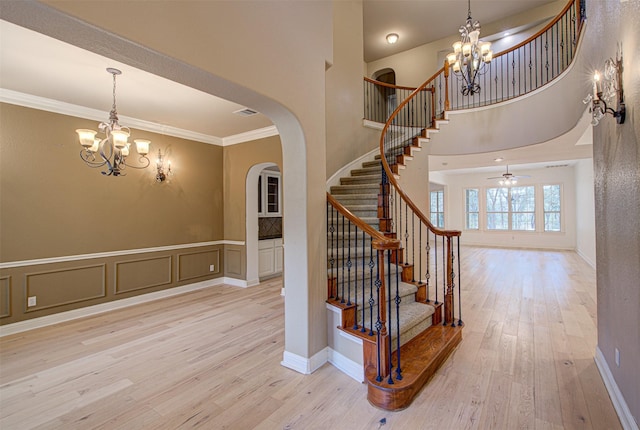 stairway with crown molding, wood-type flooring, and ceiling fan with notable chandelier