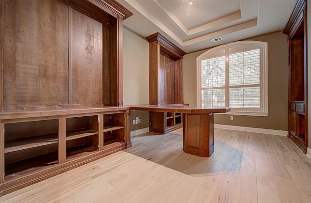 unfurnished office featuring built in desk, crown molding, a raised ceiling, and light wood-type flooring