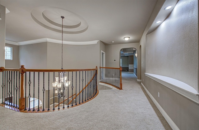 corridor featuring an inviting chandelier, crown molding, a tray ceiling, and carpet