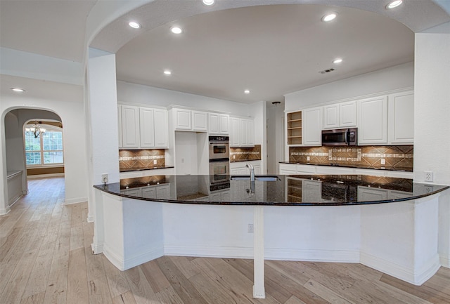 kitchen with sink, light hardwood / wood-style flooring, dark stone countertops, appliances with stainless steel finishes, and white cabinets