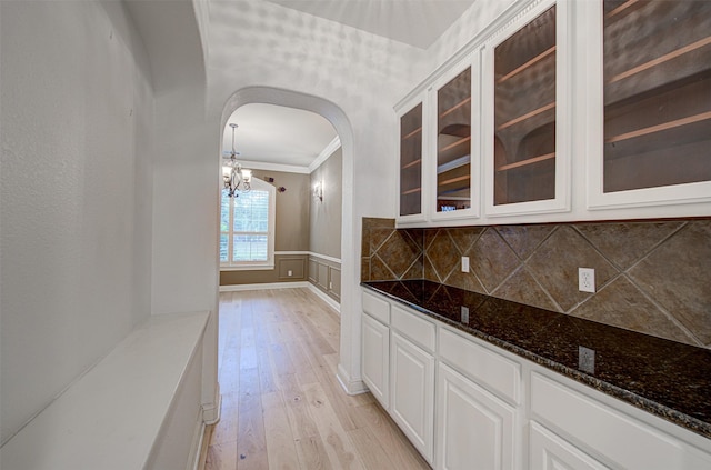 interior space with light hardwood / wood-style flooring, hanging light fixtures, ornamental molding, white cabinets, and dark stone counters