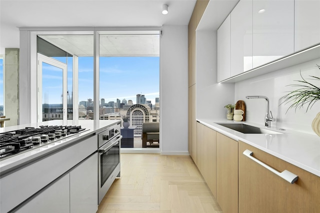 kitchen with white cabinetry, stainless steel appliances, sink, and light parquet floors