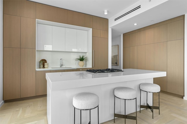 kitchen with stainless steel gas cooktop, sink, a center island, white cabinets, and light parquet floors