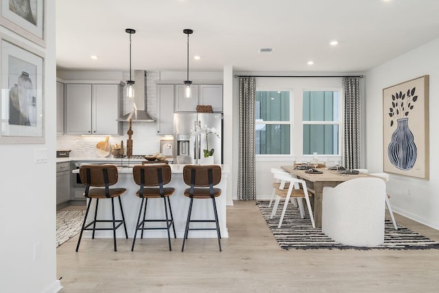 kitchen with a center island, decorative backsplash, stainless steel fridge with ice dispenser, decorative light fixtures, and wall chimney exhaust hood